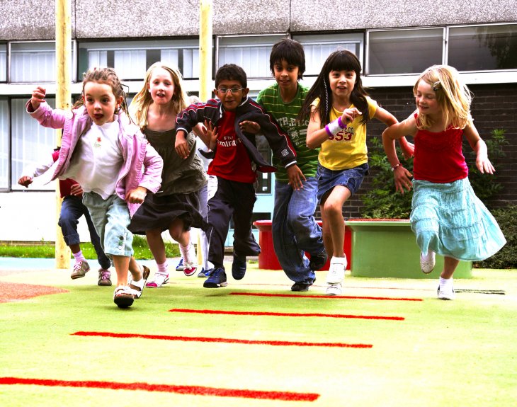 Mehrere Kinder laufen über ein Teppichvlies auf einem Spielplatz.